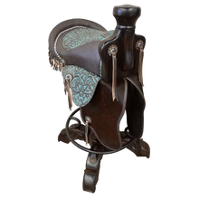Load image into Gallery viewer, The Mustang Saddle Barstool features embossed turquoise leather, full-grain leather panels, and a hand-forged medallion on a 180° swivel wood base. A handcrafted Western saddle barstool celebrating the artistry and heritage of the American West.