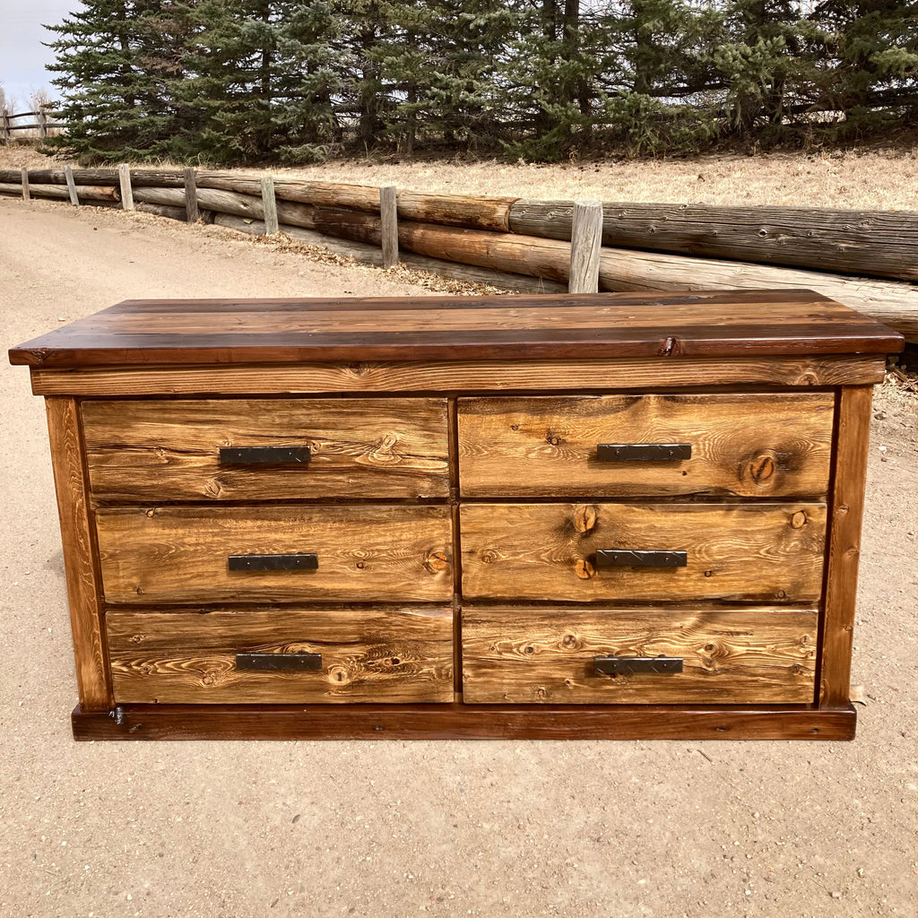 A rustic lowboy dresser made of ponderosa pine with hand forged iron pulls, placed outdoors against a natural backdrop.