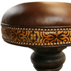 The El Matador Bajo 5 Barstool features brown full-grain leather, hand-tooled accents, and a carved wood base with a forged iron footrest. A 360° swivel and customizable design make it a perfect blend of comfort and craftsmanship.