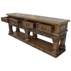 Handcrafted Spanish colonial console with baroque floral scroll carvings, forged iron handles, 4 drawers, platform base & antique finish. Customize your luxury Western décor piece.