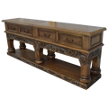Handcrafted Spanish colonial console with baroque floral scroll carvings, forged iron handles, 4 drawers, platform base & antique finish. Customize your luxury Western décor piece.