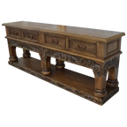 Handcrafted Spanish colonial console with baroque floral scroll carvings, forged iron handles, 4 drawers, platform base & antique finish. Customize your luxury Western décor piece.
