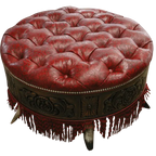 Handcrafted red leather ottoman with carved wood base, nailhead trim, and fringe detailing. The Coronado Ottoman blends Western luxury with timeless artisan craftsmanship.
