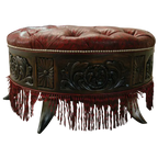 Handcrafted red leather ottoman with carved wood base, nailhead trim, and fringe detailing. The Coronado Ottoman blends Western luxury with timeless artisan craftsmanship.