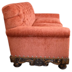 Handcrafted Western loveseat with carved wood base, rust-toned fabric, and tufted backrest. The Durango Loveseat blends rustic warmth with refined craftsmanship. Customizable.